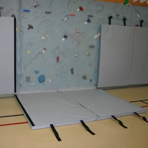 gray climbing wall mats by sportsfield specialties hooked to the climbing wall protecting gym users from hitting climbing holds
