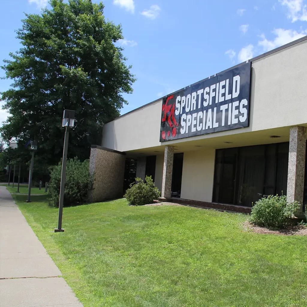 front of the sportsfield specialties office with a large metal sign with the logo on it