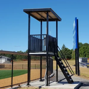 a black elevated filming tower installed along the outfield fence of a playing field