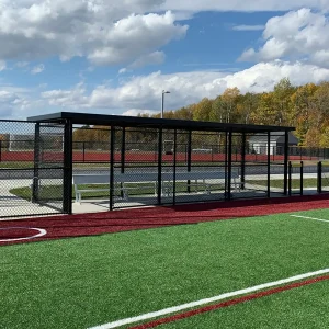 a black GameShade® dugout installed on the side of a synthetic turf playing field along with aluminum team benches