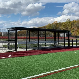 A black GameShade® Dugout installed on a turf ball field with aluminum team benches