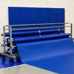 a blue gym floor cover being rolled into a storage rack at the end of a gymnasium
