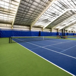 internal wind tennis net systems installed at an indoor tennis court with a green and blue playing surface