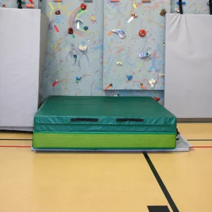 a portable landing zone pad sitting on a gym floor up against a climbing wall