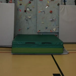 Green portable landing zone mat by Sportsfield Specialties laid out below climbing wall