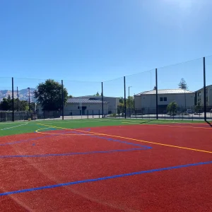 pole to pole tension netting system installed between a synthetic turf playing field and a row of buildings