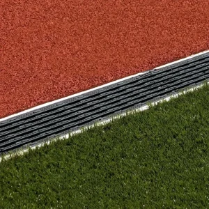 a precast trench drainage system by ACO® installed between a track surface and synthetic turf to prevent water run off from flooding the playing field