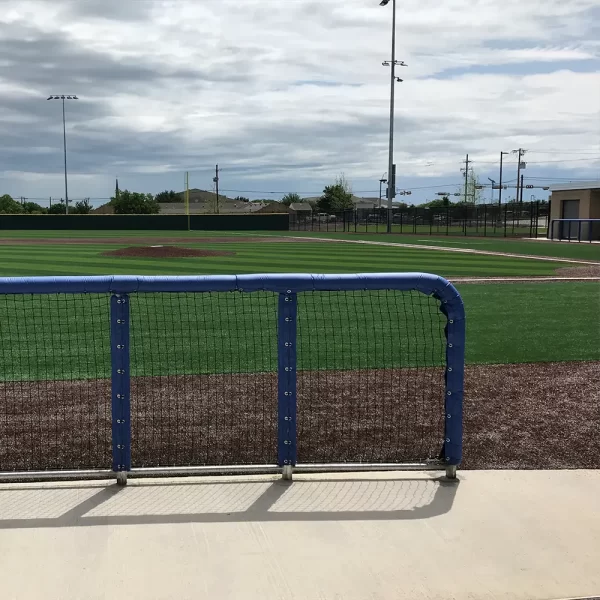 looking through green round guard rail padding out into the softball field