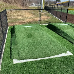two seasonal bullpen pitching mounds sitting in the practice area of a multi-purpose athletic field