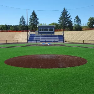 a turf covered portable pitching mound facing home plate, bleachers and press box