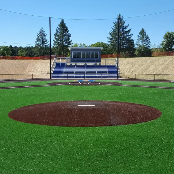 a turf covered portable pitching mound facing home plate, bleachers and press box