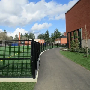 a black semi-permanent fence system installed between a playing field and school building